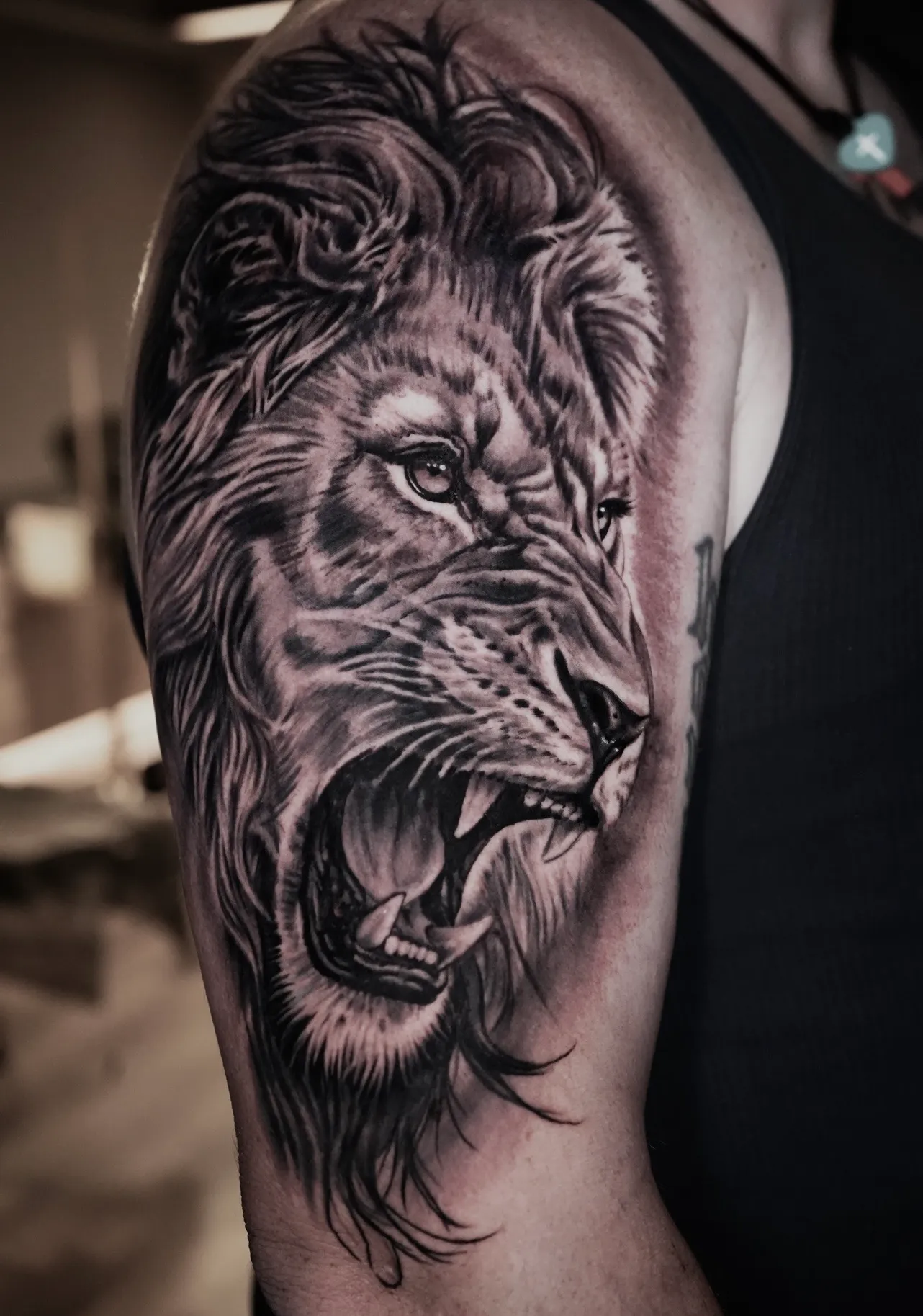 Black and grey realism roaring lion upper arm tattoo by Bishop Kelly