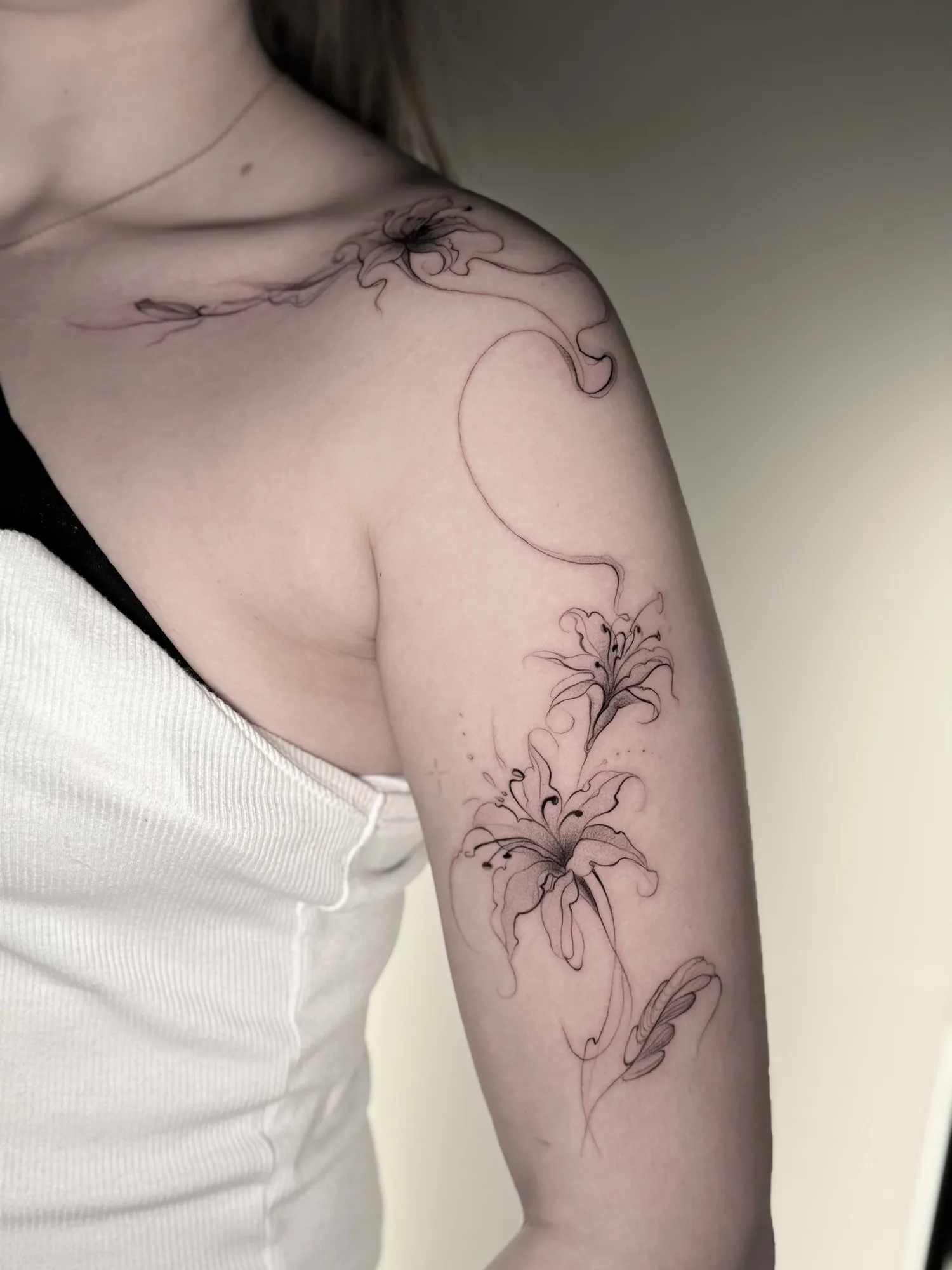 Fine line spider lily shoulder tattoo by Keisha Vo